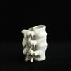 A white ceramic vase shaped like vertebrae is photographed against a black background.