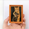 A framed painting featuring two cats, one orange and one black, displayed in a wooden frame.