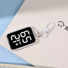 A white LED keychain pocket watch with a digital display showing 2:05 PM resting on a light-colored surface.
