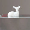 A white resin ornament shaped like an elk or deer, displayed on a glass surface.