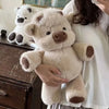 A person is holding a light beige Highland cow plush toy next to another white plush toy.