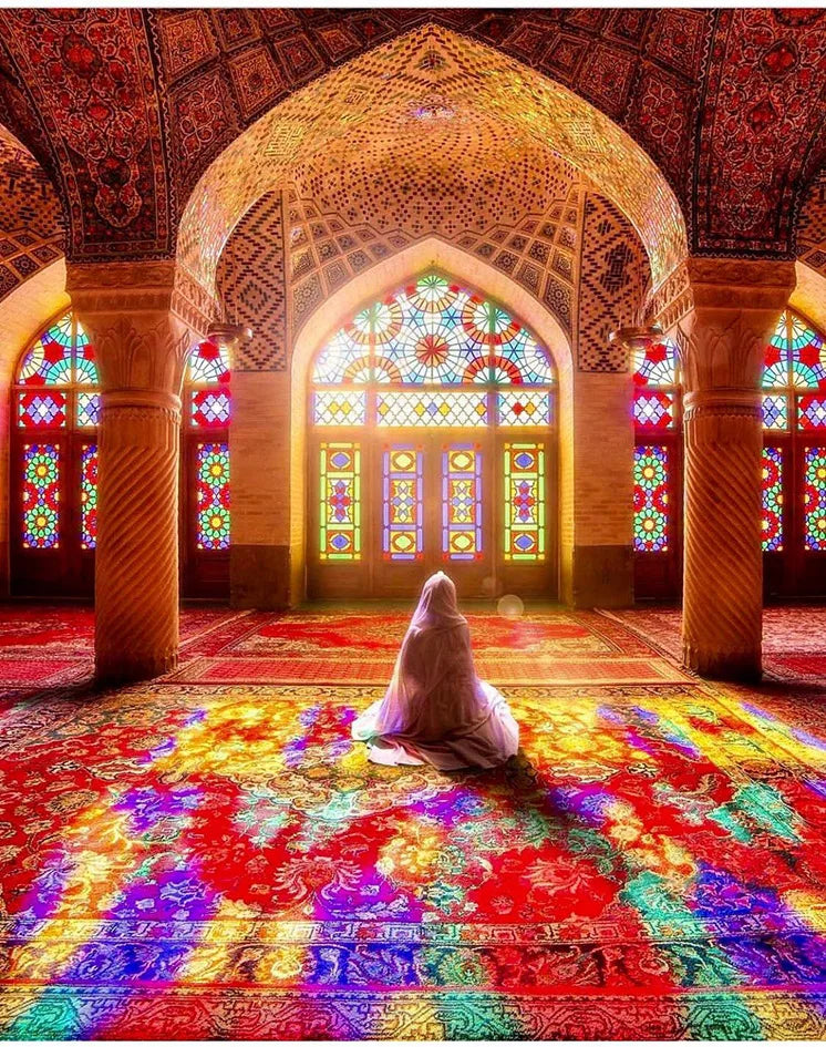 Islamic mosque interior with an arched dome and stained glass windows, featuring vibrant red and gold patterns on the floor.