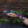 A hand holds a vibrant, color-changing flexible dragon figurine against a dark wooden background.