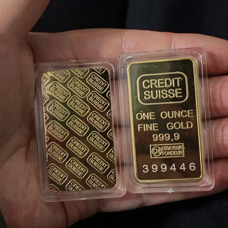 A hand holds two clear plastic sealed gold bullion ingots labeled Credit Suisse with the inscription ONE OUNCE FINE GOLD 999.