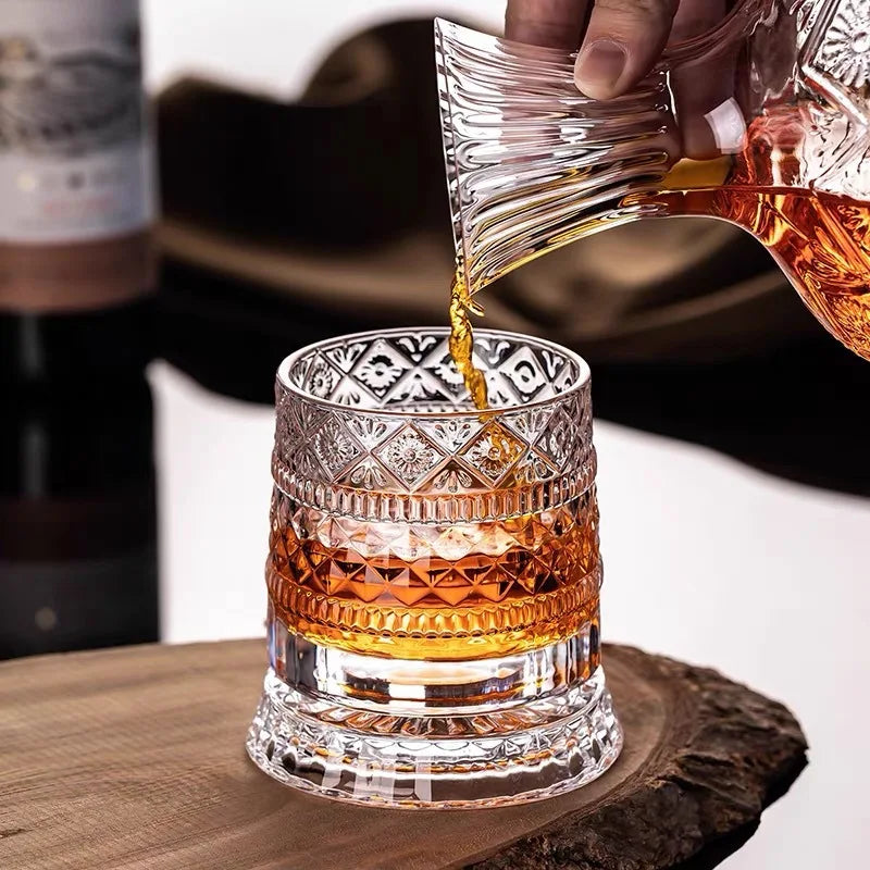 A hand pours amber liquid into a rotating crystal whiskey glass with relief design.