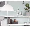 A silver resin balloon dog sculpture sits on a white shelf next to a potted green tree and a white lampshade.