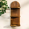 A vertical wooden wall shelf with a curved, ribbed design mounted on a white wall next to green foliage.