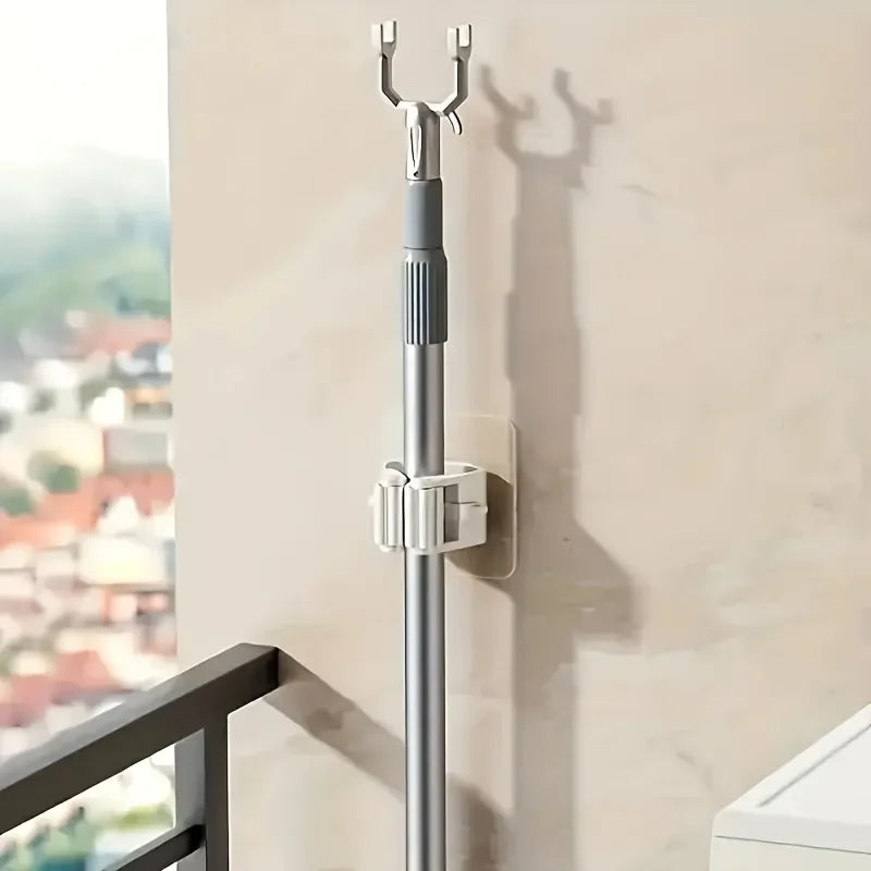 A silver wall mounted holder for a mop and broom, attached to a light-colored wall.