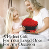 A woman is presenting a bouquet of red roses in a black heart-shaped gift box to a young girl.