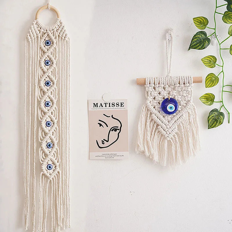 Macrame wall hanging featuring a long fringe and an evil eye pendant on a wooden hanger.