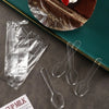 Clear plastic disposable spoons arranged on a dark surface next to a cake and foil.