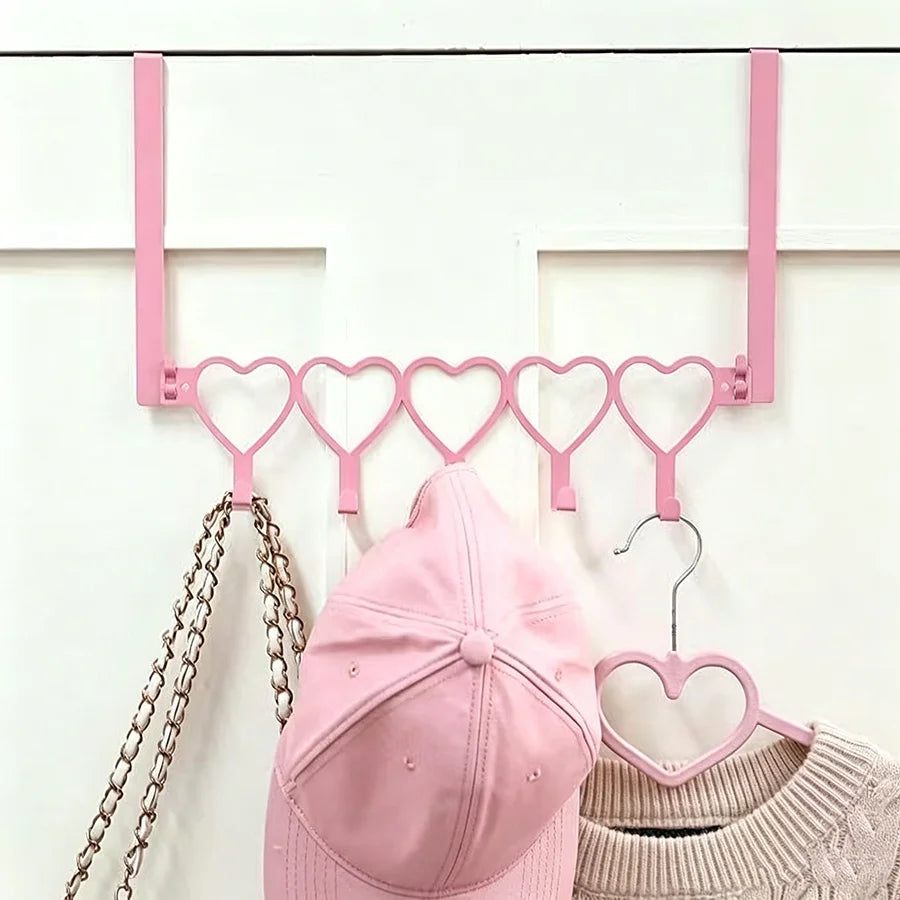 Pink heart over-the-door hook rack with five pink heart shaped hooks mounted on a white door frame.