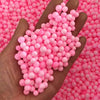 A hand holds a large quantity of pink foam beads against a background of similar colored beads.