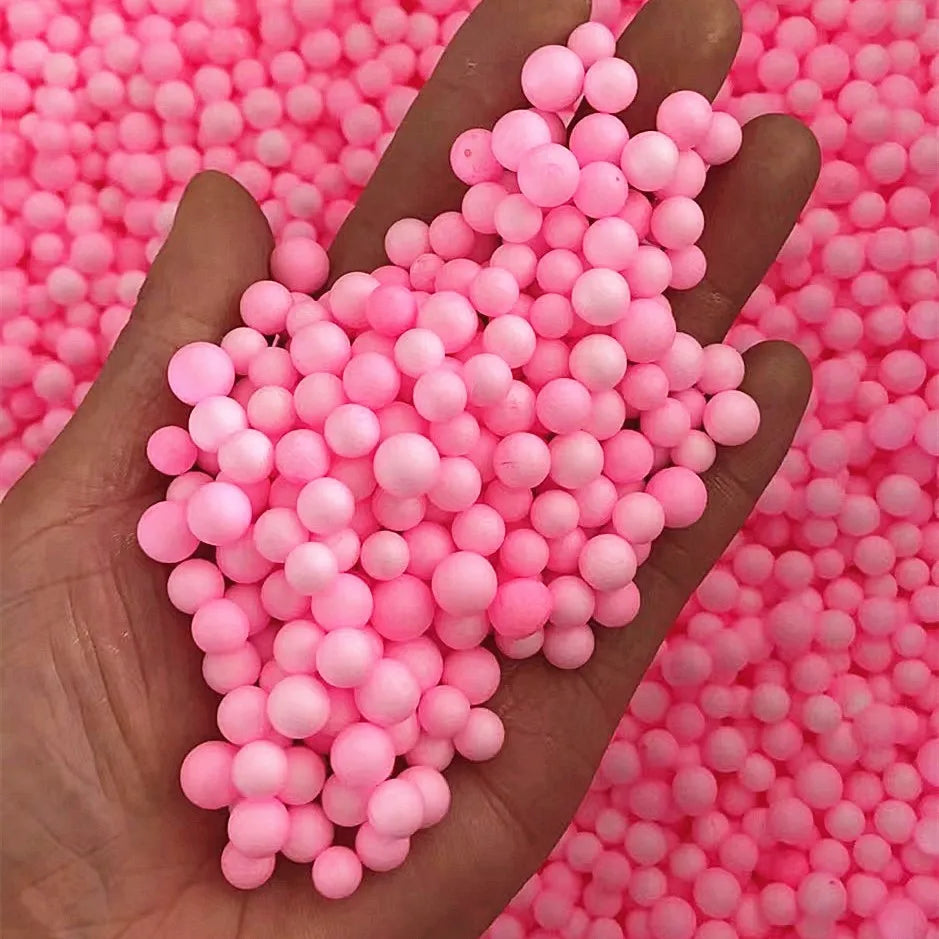 A hand holds a large quantity of pink foam beads against a background of similar colored beads.