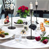 A table setting featuring three metal taper candle holders with white candles and a plate of food.
