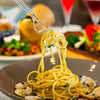 A clear plastic dessert fork is lifting a bundle of yellow spaghetti noodles from a bowl.