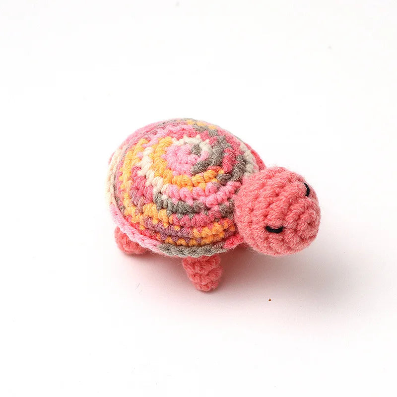 Handmade crocheted turtle plush with a multicolored, striped shell and pink feet.