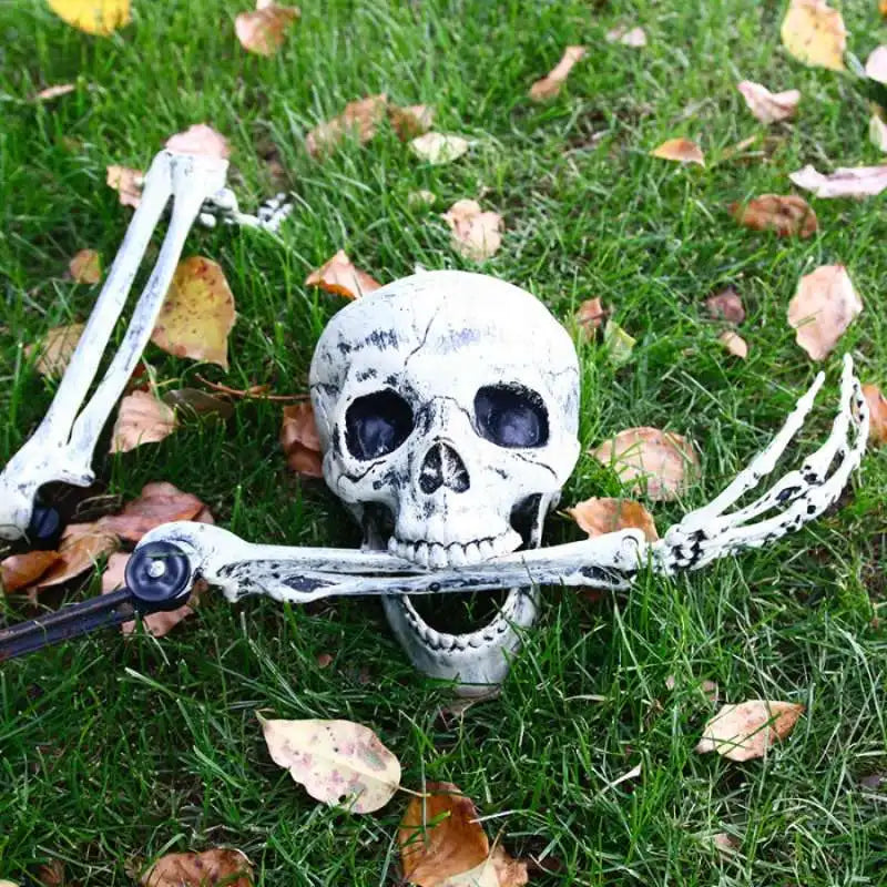 A realistic white skeleton arm stake lying on green grass amidst fallen autumn leaves.