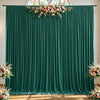 A dark emerald green fabric backdrop with vertical pleats decorated with a floral arrangement above and below.