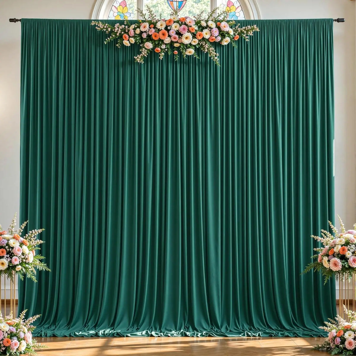 A dark emerald green fabric backdrop with vertical pleats decorated with a floral arrangement above and below.
