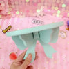 A hand holds a light blue decorative bow-shaped wooden shelf against a pink background.