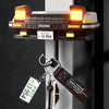 A classic car headlight key holder with LED illumination mounted on a wall, featuring a brass tag and leather strap.
