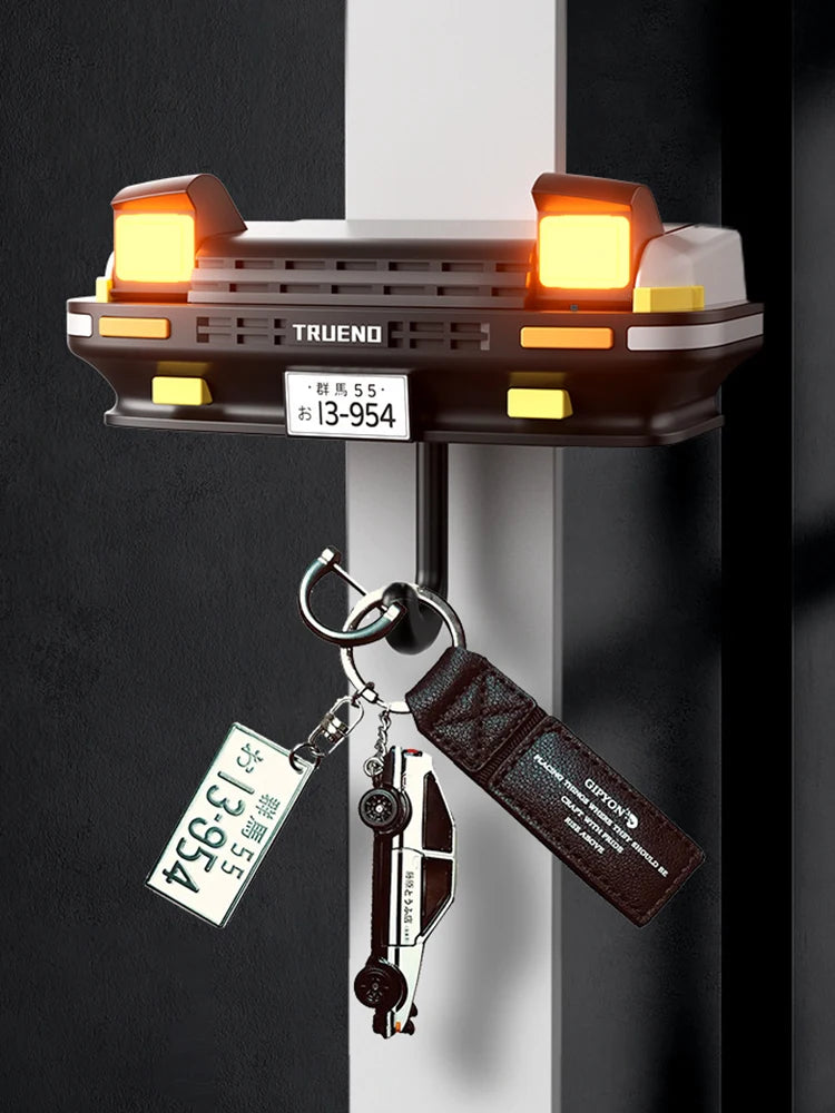 A classic car headlight key holder with LED illumination mounted on a wall, featuring a brass tag and leather strap.