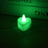 A glowing green heart-shaped LED tealight candle resting on a dark wooden surface.