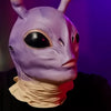 A close-up of a purple alien full-face latex mask with large black eyes and pale skin, worn by a person.