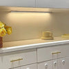 Under-cabinet lighting illuminates a countertop with a yellow flower and a ceramic cup in a modern kitchen cabinet.