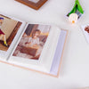 An open photo album displaying a portrait of a child, next to a green flower and a wooden frame.