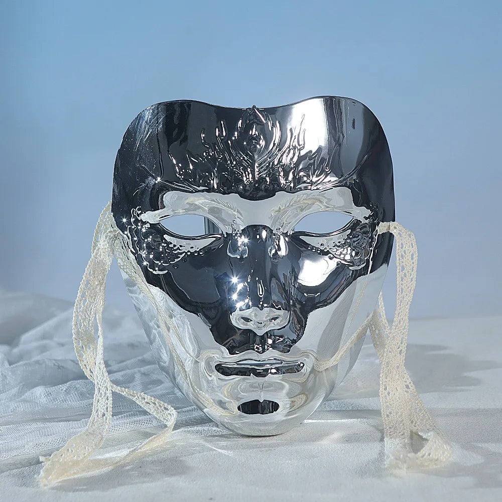 A silver, translucent masquerade mask with a fierce animalistic face design is displayed on white fabric.