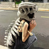 A person wearing a wearable dinosaur skeleton costume with a head and spine, posing outdoors.