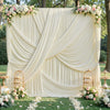 A white draped curtain backdrop decorated with floral garlands and greenery for a wedding or event.
