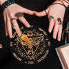 Hands holding a black wooden pendulum board with gold accents and a rose quartz crystal necklace
