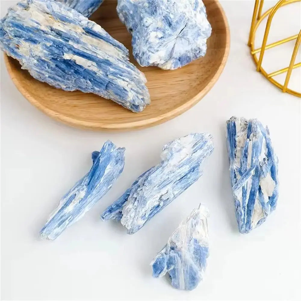 Several pieces of blue kyanite crystal stone are displayed on a wooden plate and white surface.