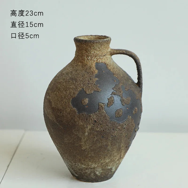 A dark brown ceramic vase with a handle and irregular black markings, shown from the side.