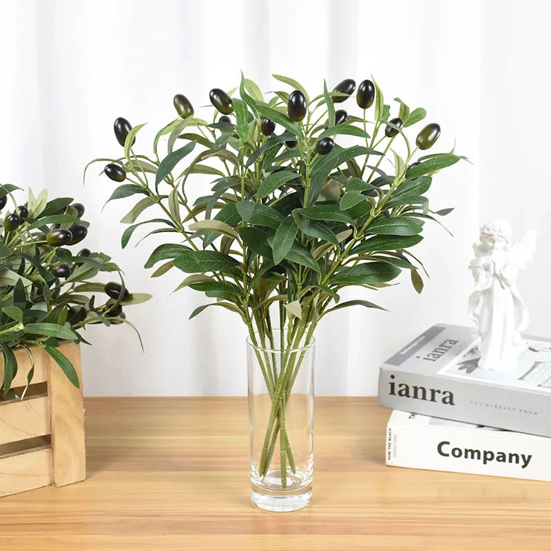 Artificial olive leaf branch with dark green leaves and small black olives in a clear glass vase