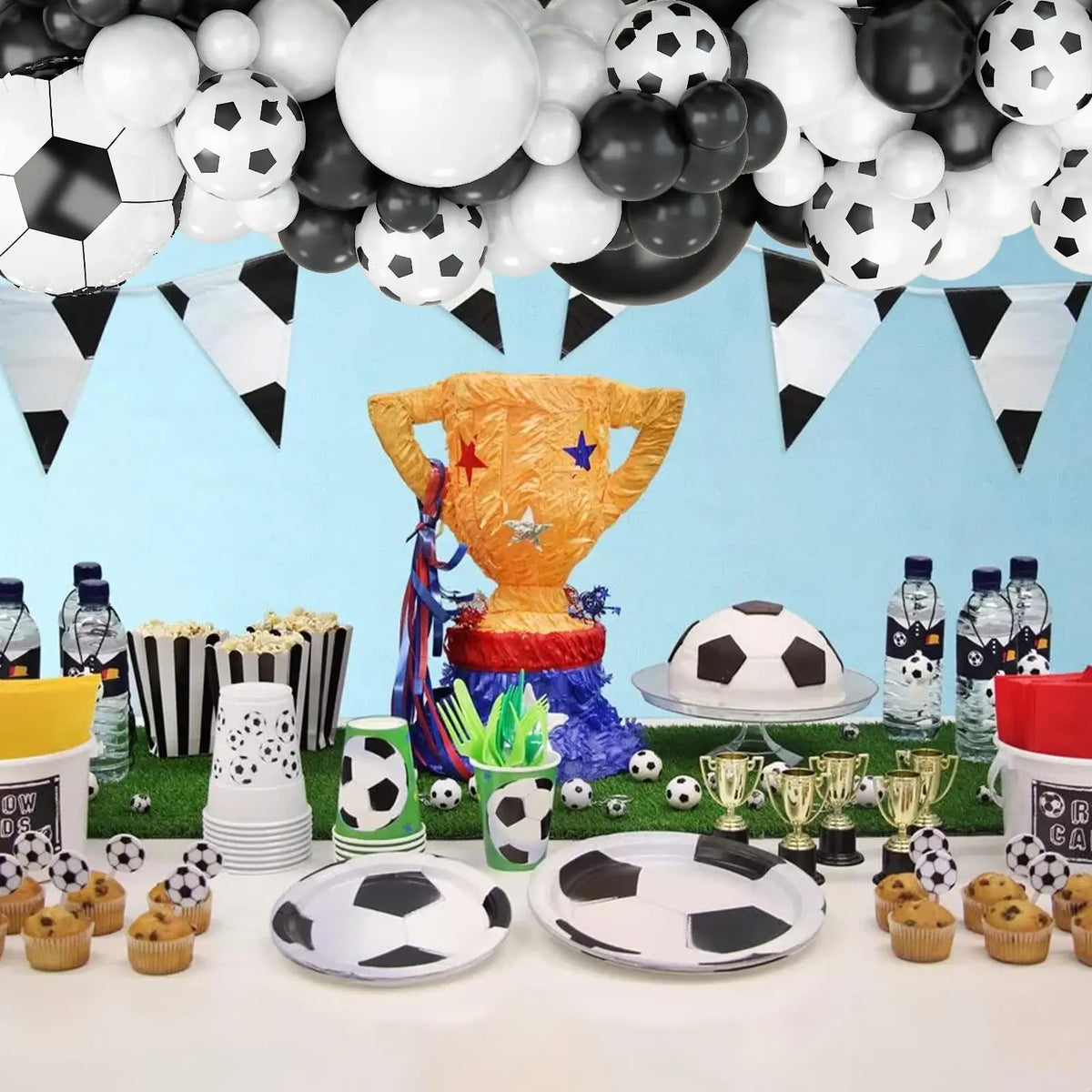A decorative display featuring a golden soccer trophy, various black and white balloons, and soccer balls arranged for party 