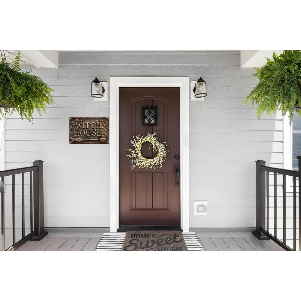 A dark brown wooden door with a decorative wreath and a vintage witch house metal sign above it, set in a light gray exterior