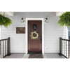 A dark brown wooden door with a decorative wreath and a vintage witch house metal sign above it, set in a modern gray exterio