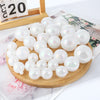 A wooden plate holds a cluster of white pearl-like balloon cake toppers for party desserts.