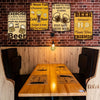 A set of four vintage metal signs featuring humorous pub art about beer and drinking displayed on a brick wall above a wooden