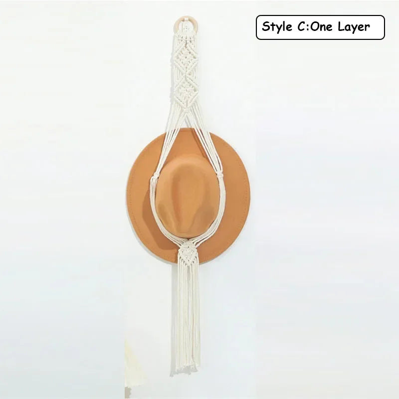 A light beige macrame hat organizer with a wooden dowel is shown against a white background.