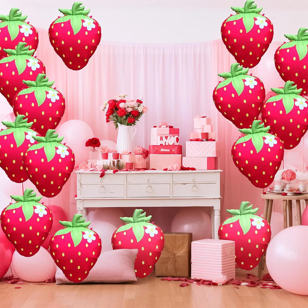Pink and red strawberry foil balloons decorating a party backdrop with pink drapery and gifts
