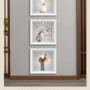 Affichage de trois pots décoratifs encadrés avec des arrangements floraux séchés sur un mur gris clair.