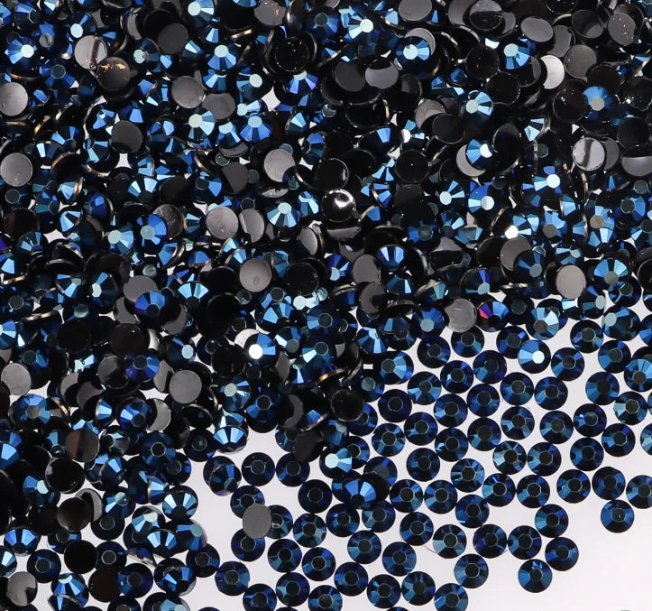 A close-up view of dark blue and black flatback resin rhinestones scattered on a white background.