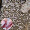 Close-up of iridescent nail rhinestones scattered on a textured surface with a hand displaying pink glitter nails.