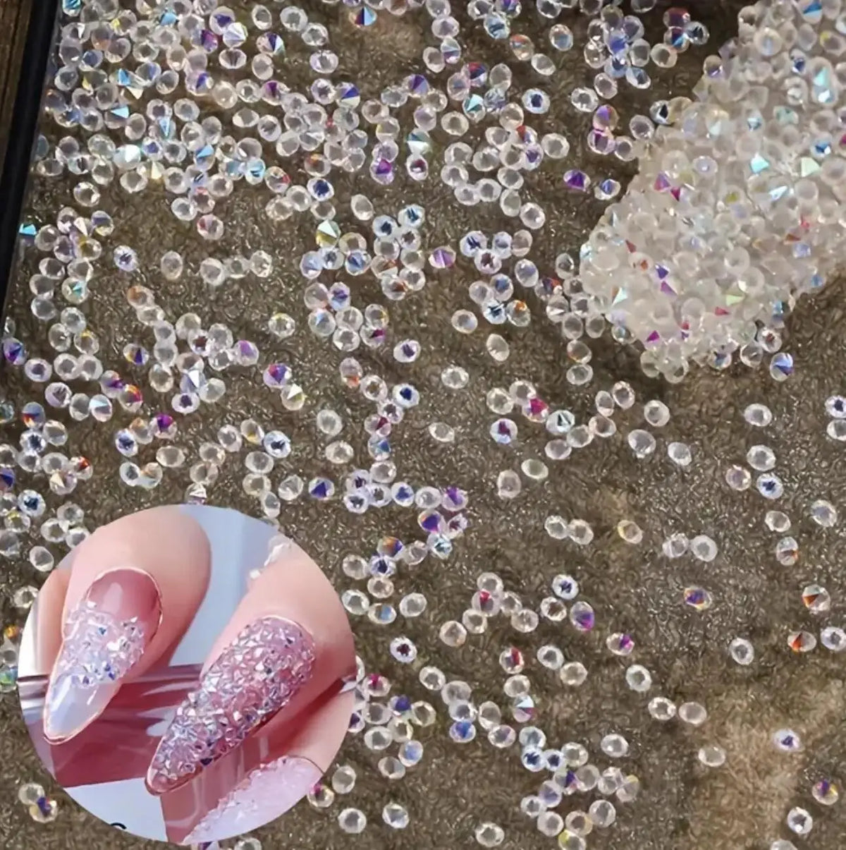 Close-up of iridescent nail rhinestones scattered on a textured surface with a hand displaying pink glitter nails.