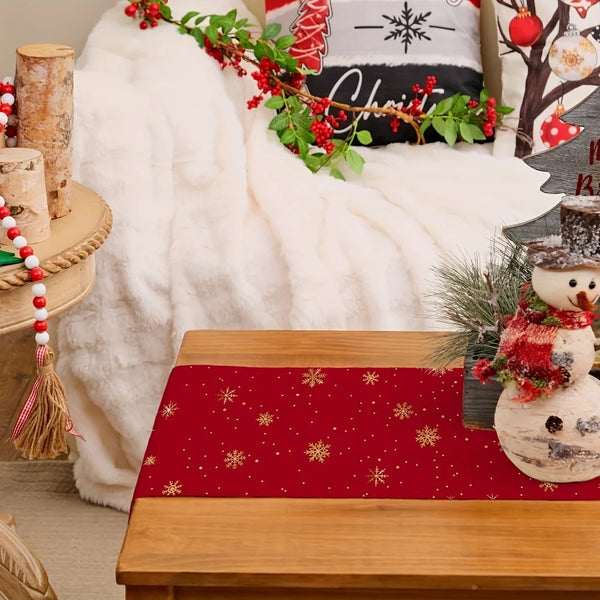 A festive Christmas table runner in red with gold snowflakes is displayed on a wooden table.